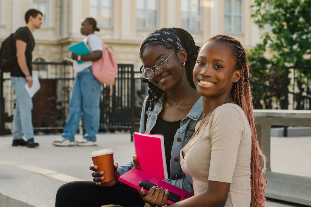 Primer plano de chicas universitarias diversas sentadas en las escaleras del campus, sonriendo y charlando